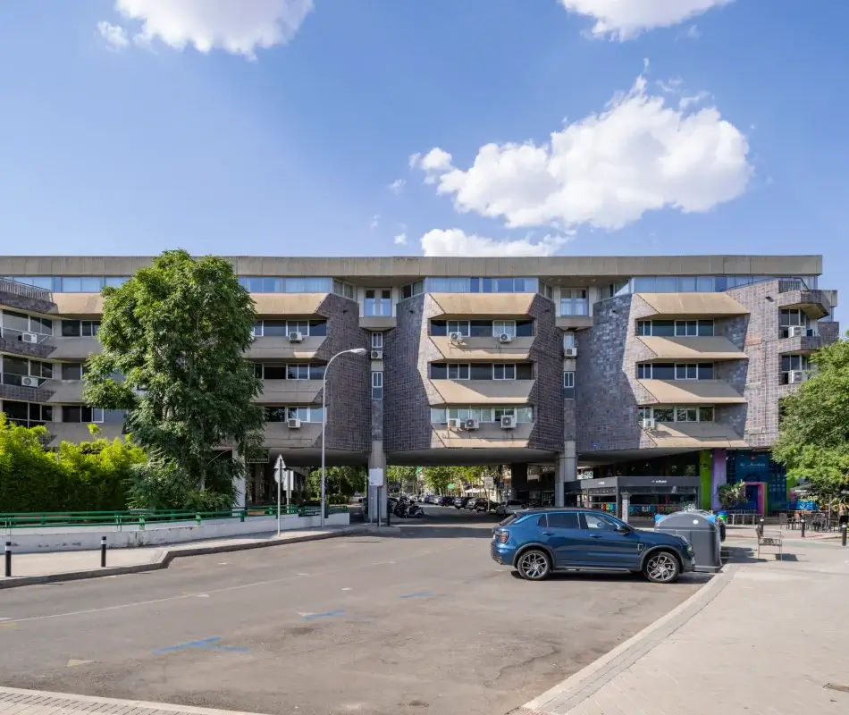 Edificio de oficinas con estacionamiento, &aacute;rboles y autos bajo cielo despejado