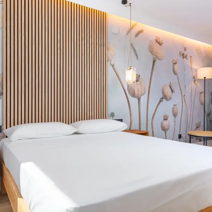 Habitaci&oacute;n moderna con cama blanca y pared decorada con flores tipo diente de le&oacute;n.