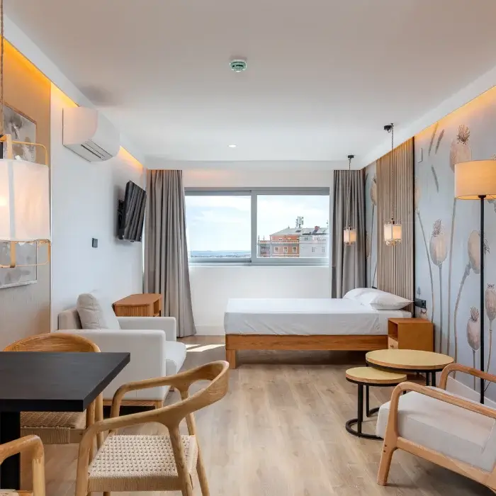 Interior de habitaci&oacute;n de hotel moderna, cama y zona de estar con ventana.