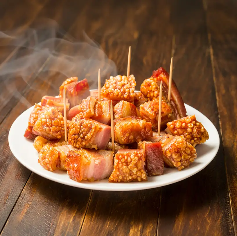Plato con bacon y carne caramelizada con brochetas y humo sobre madera