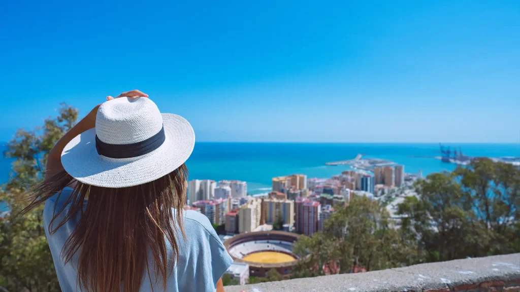 Mujer con sombrero blanco, mirando la ciudad y el mar azul desde un mirador