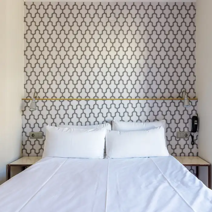 Habitaci&oacute;n con cama con s&aacute;banas blancas y pared con patr&oacute;n geom&eacute;trico.