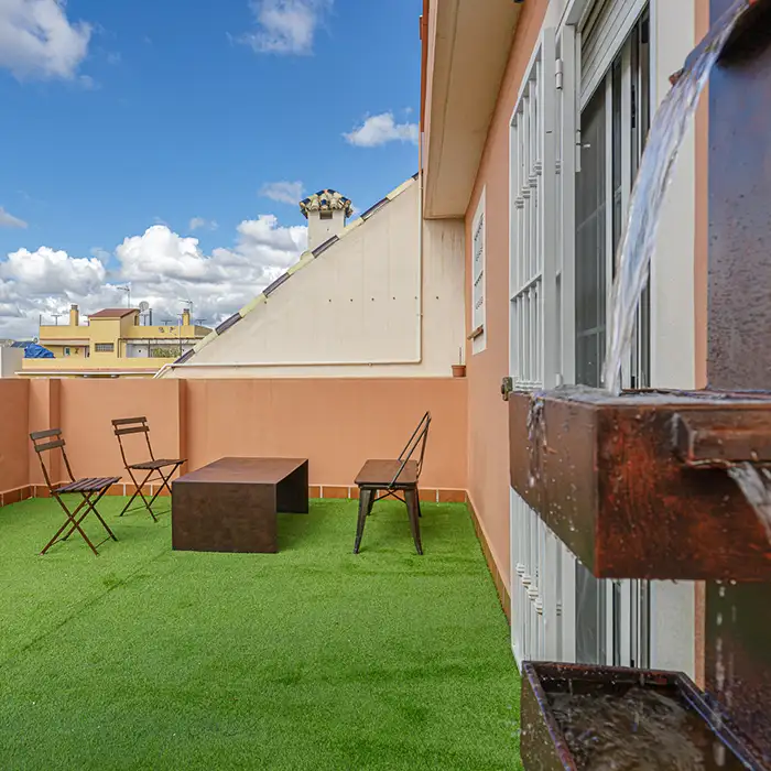 Patio con c&eacute;sped verde, sillas plegables y mesa frente a un edificio.