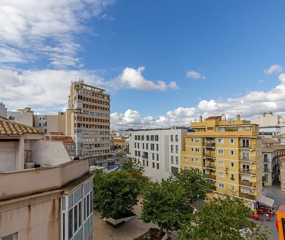 Vista urbana con edificios de viviendas y &aacute;rboles, bajo cielo azul con nubes.