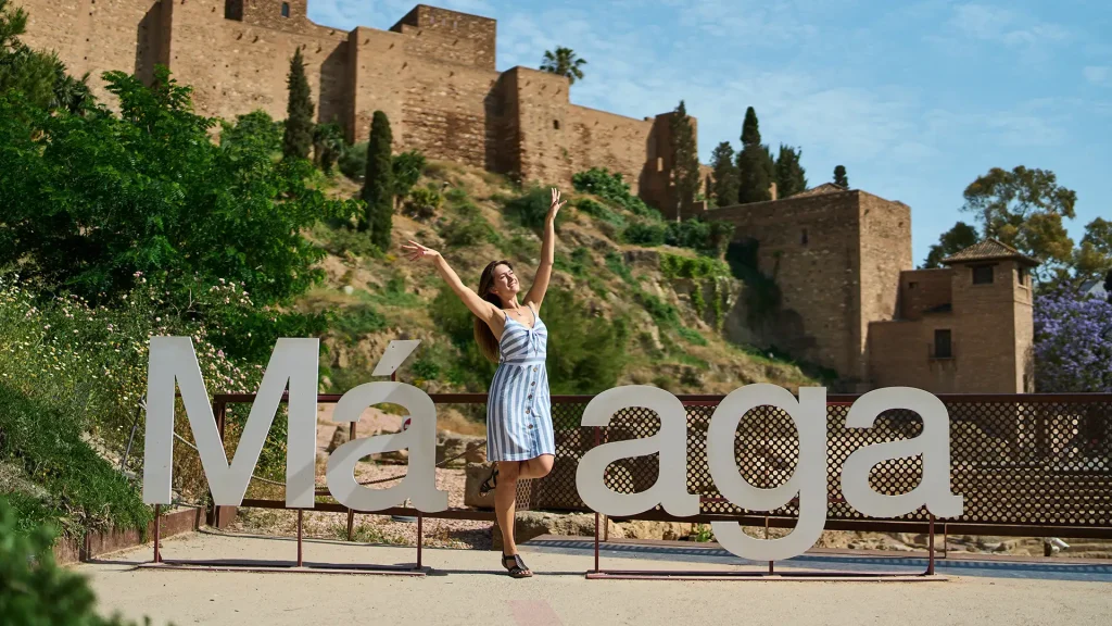 Mujer sonriente posa con los brazos arriba frente a letrero &ldquo;M&aacute;laga&rdquo;