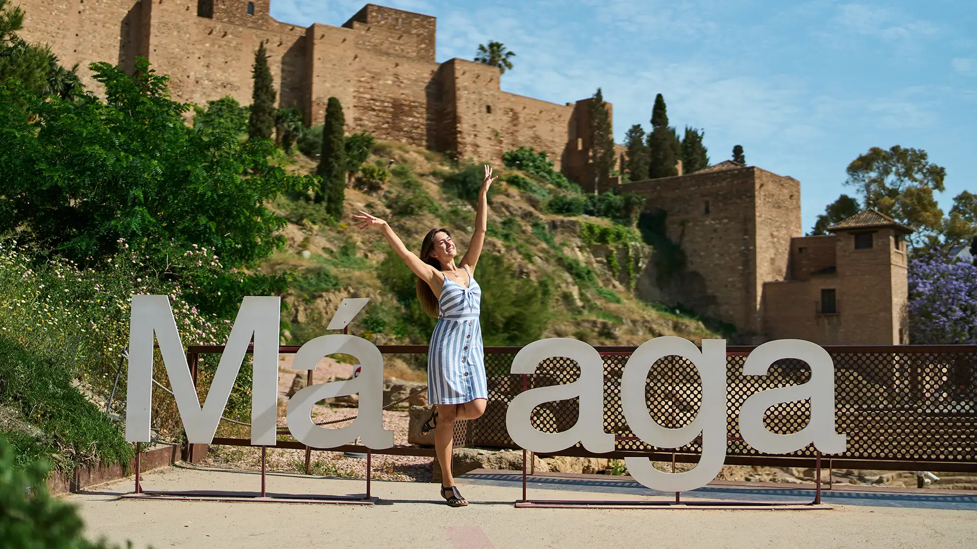 Mujer posa con los brazos arriba frente al letrero &ldquo;M&aacute;laga&rdquo;, junto al castillo