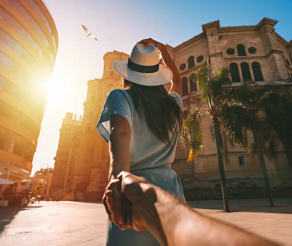 Mujer con sombrero frente a un templo antiguo al atardecer, con mano saludando
