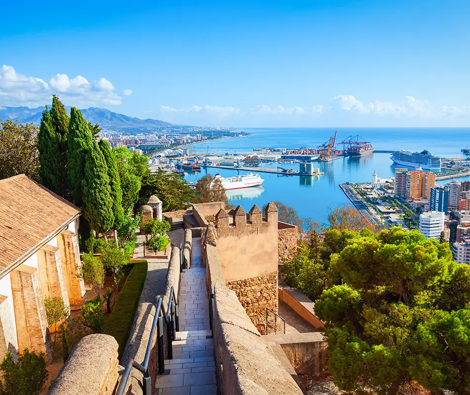 Escaleras y murallas en colina, puerto con barcos y ciudad al fondo