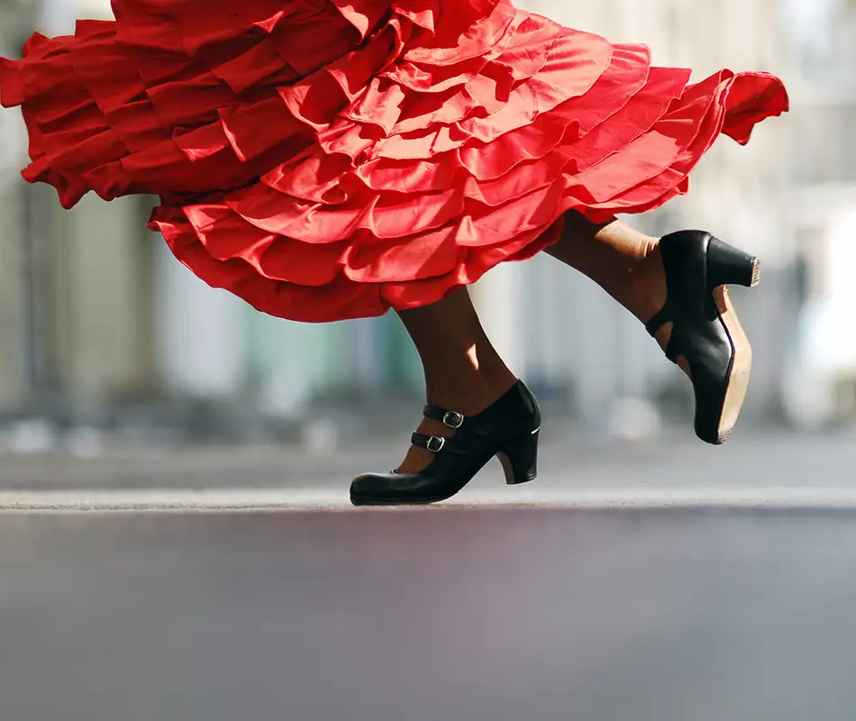 Bailarina con vestido rojo y botas negras saltando en una calle.