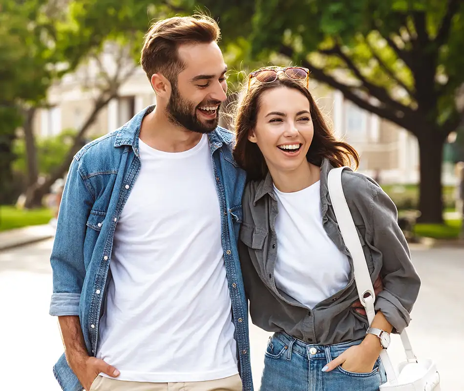 Pareja de j&oacute;venes sonrientes paseando en un parque con mochilas y ropa casual