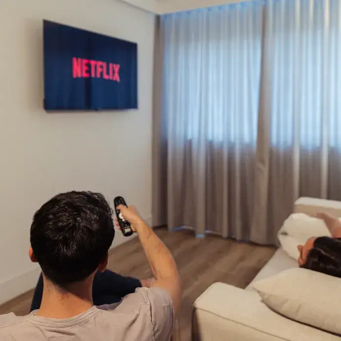 Persona frente a sof&aacute; usando el control, TV con logo de Netflix.