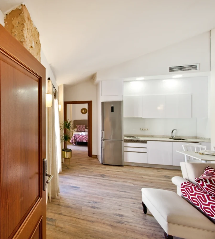 Interior de apartamento moderno con cocina blanca y sala con sof&aacute;.