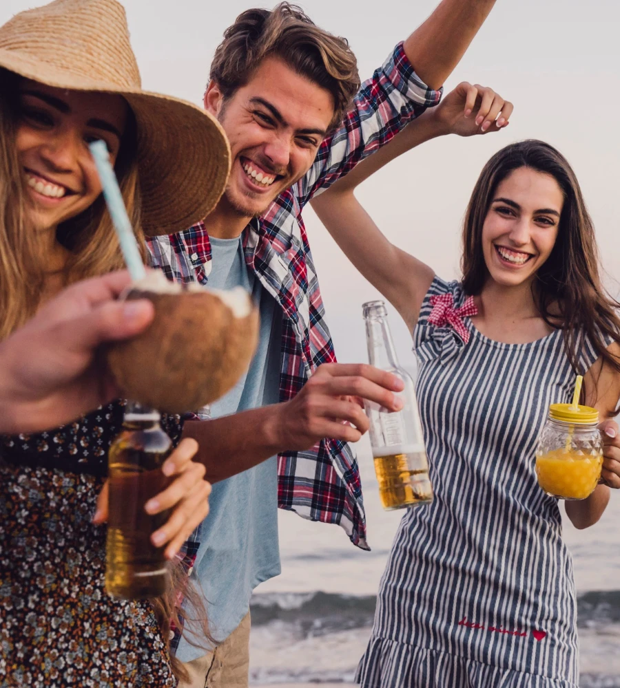 Grupo de amigos brinda en la playa con bebidas, sonriendo y levantando manos
