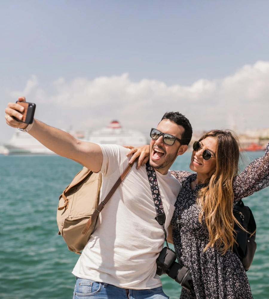 Pareja sonriente se toma un selfie en el mar con gafas de sol
