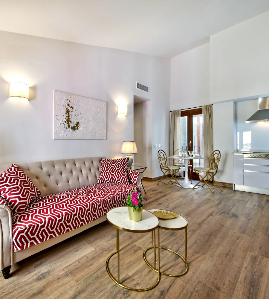 Sala de estar moderna con sof&aacute; rojo, mesa dorada y comedor al fondo.