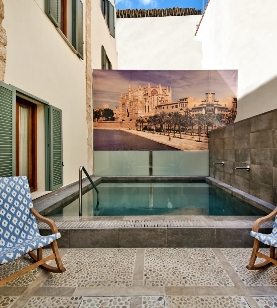 Patio con piscina rectangular, tumbonas y mural de la Catedral de Palma