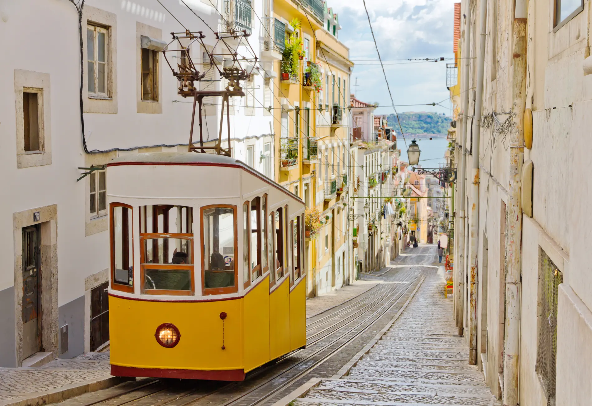 Bonde amarelo em rua estreita com pr&eacute;dios hist&oacute;ricos e fia&ccedil;&atilde;o el&eacute;trica suspensa
