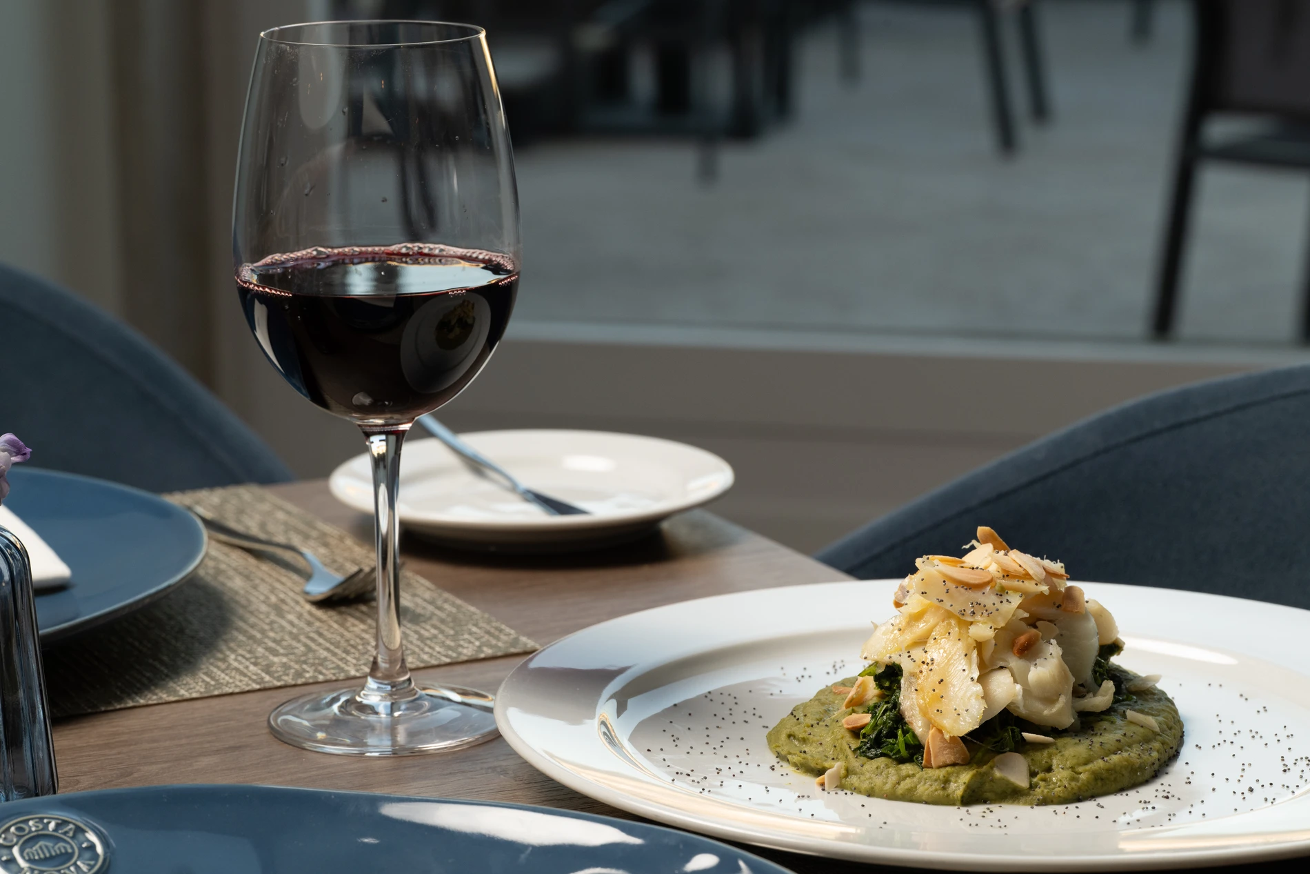 Ta&ccedil;a com vinho tinto e prato de comida em mesa ao ar livre