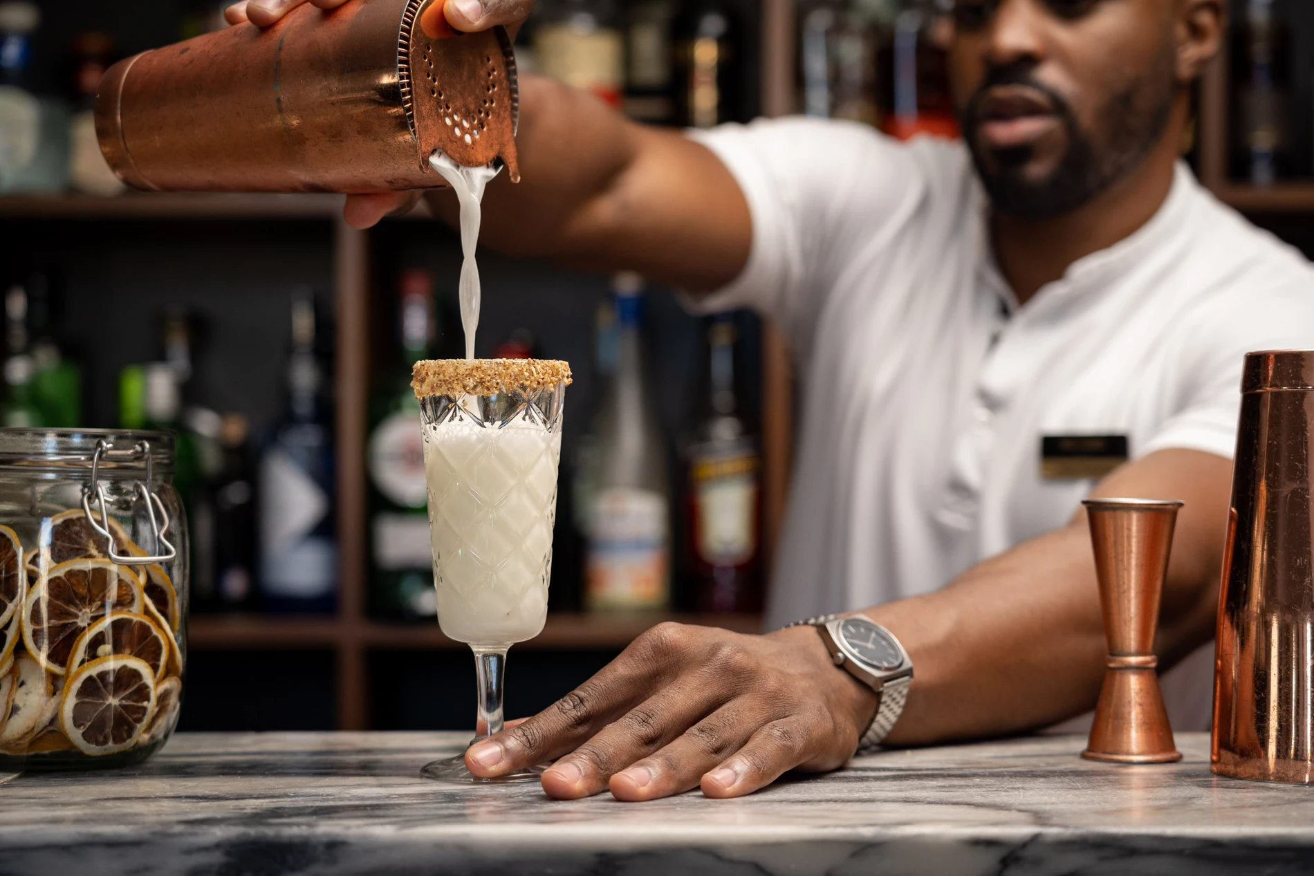 Barman serve bebida em copo, derramando leite ou creme com colher de cobre