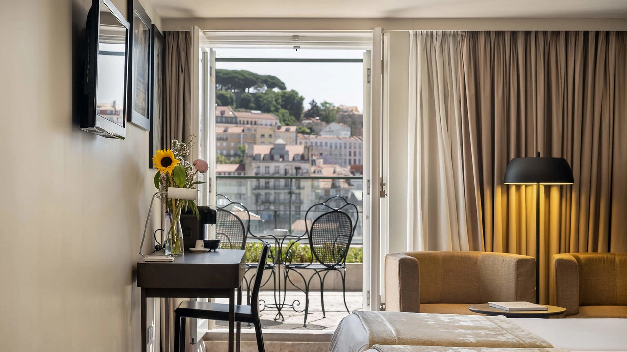 Quarto de hotel moderno com janela aberta, flores e poltronas ao fundo