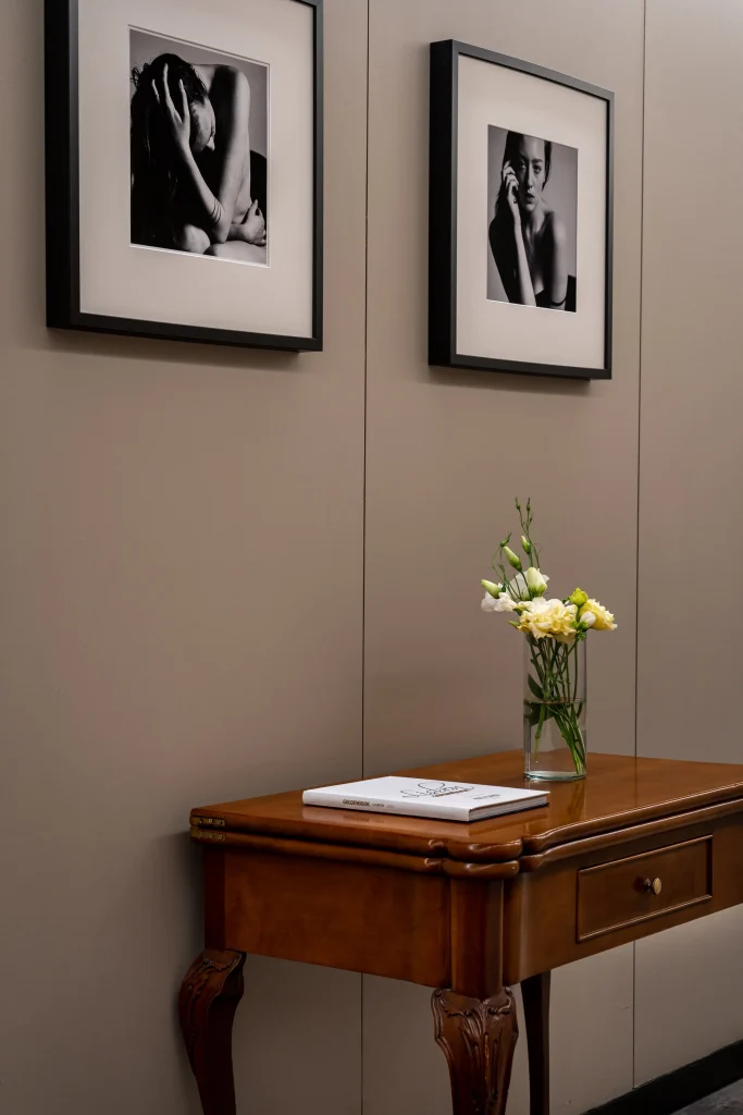 Sala com mesa de madeira, flores em vaso e dois quadros com fotos em P&B