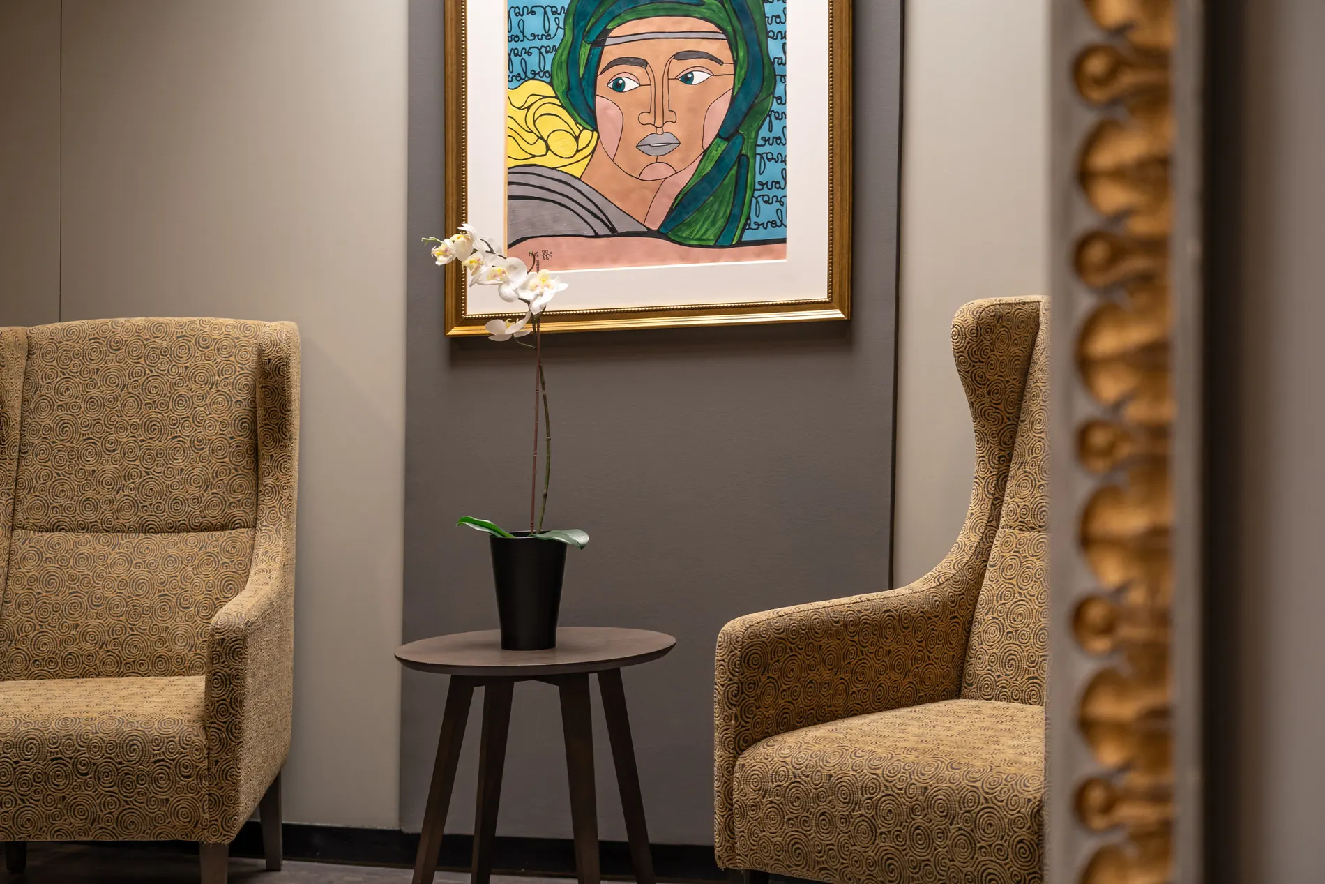 Sala decorada com poltronas estampadas, mesa lateral e quadro de mulher com len&ccedil;o verde