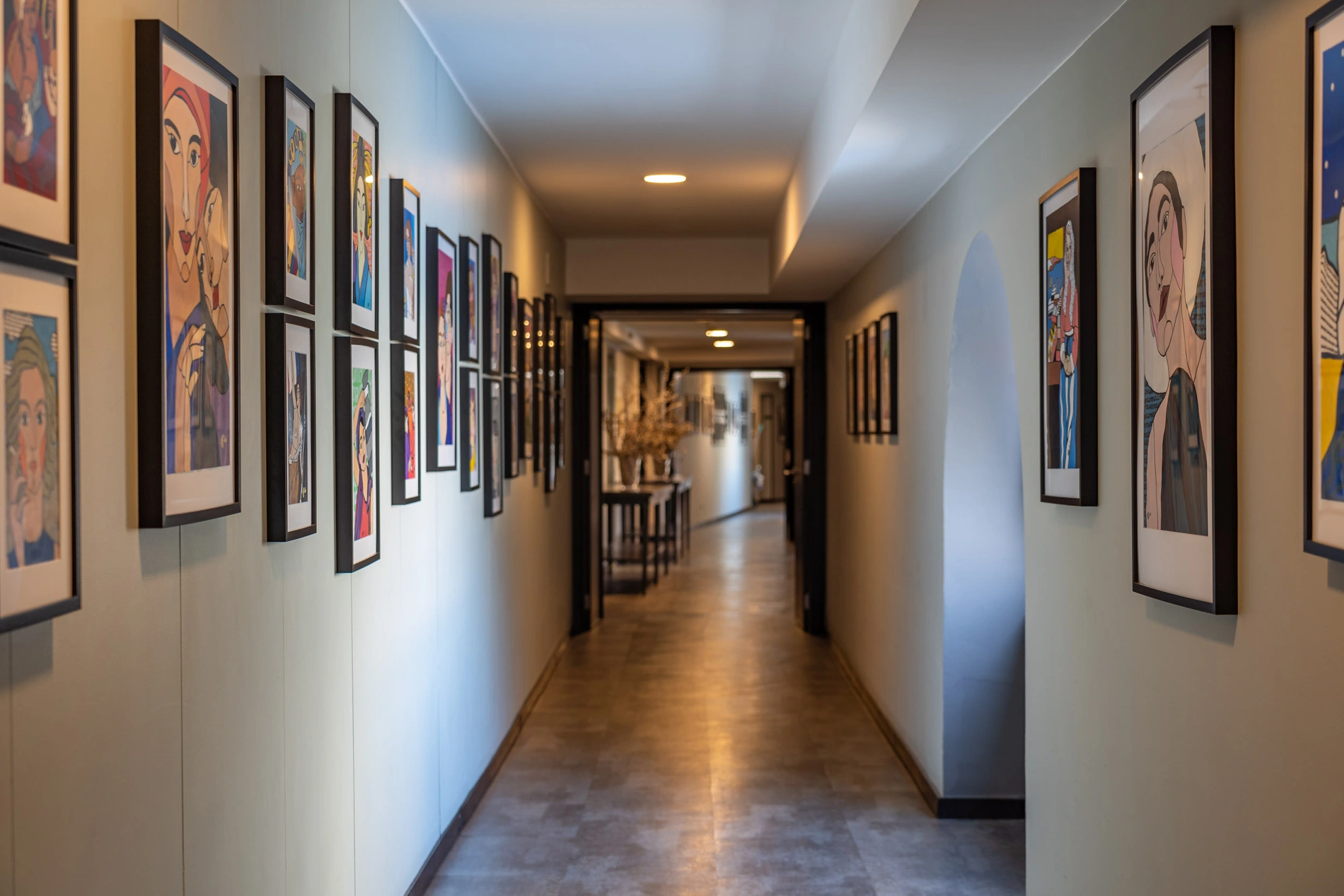 Corredor com quadros coloridos de arte nas paredes e lumin&aacute;rias no teto