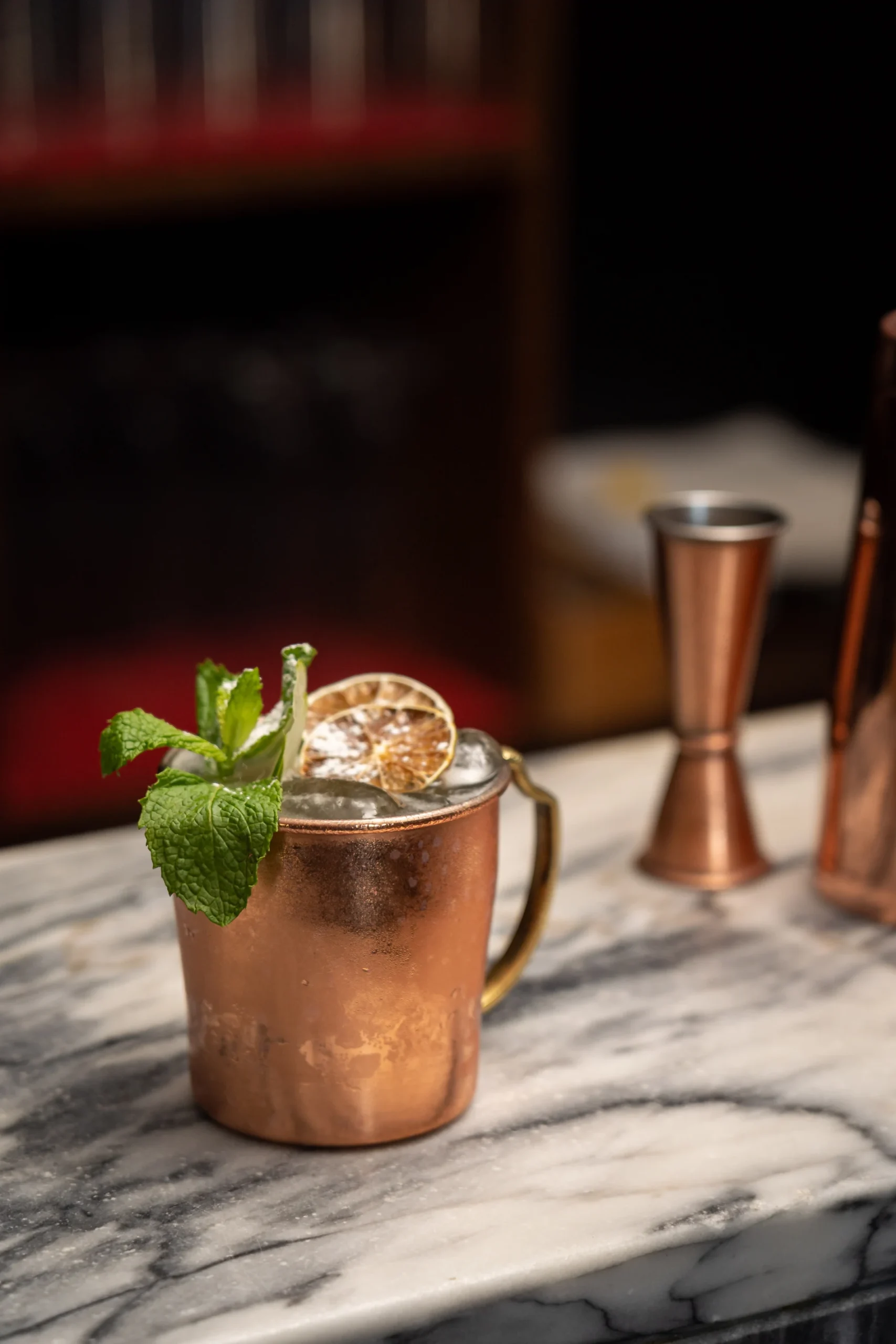 Coquetel em copo de cobre com gelo e hortel&atilde;, ao fundo barman.