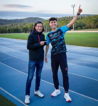 Dos j&oacute;venes sonrientes posan en una cancha de tenis, uno saluda.