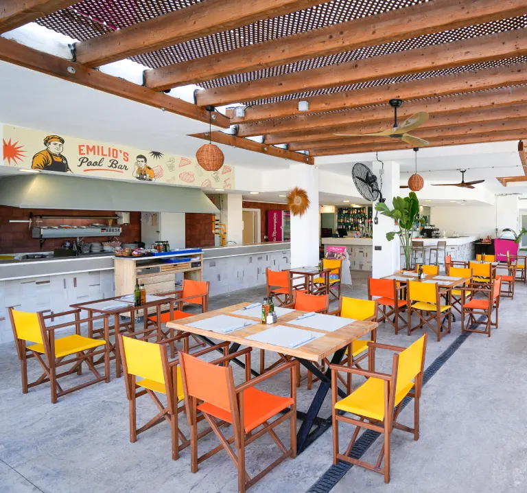 Terraza interior con mesas y sillas naranjas, barra y techo de madera.