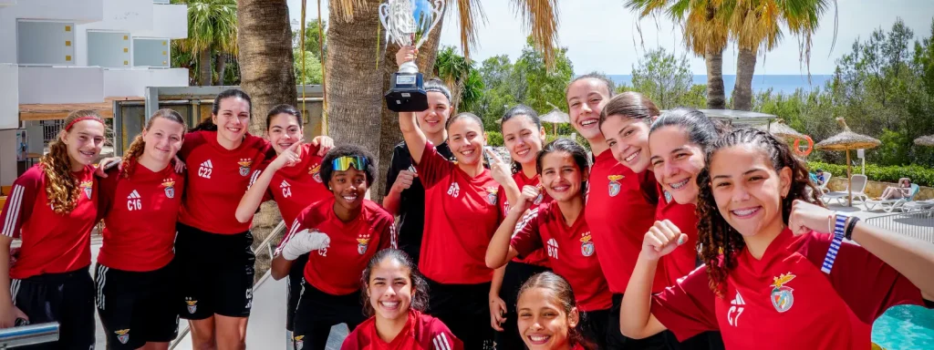 Equipo de j&oacute;venes con trofeo, posando frente a palmeras en un evento deportivo