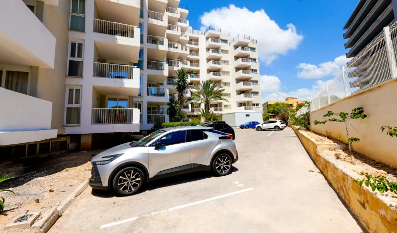 Coches y edificio residencial con balcones y palmeras bajo cielo azul