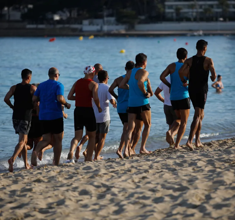 Personas corriendo y caminando en la playa junto al mar al atardecer