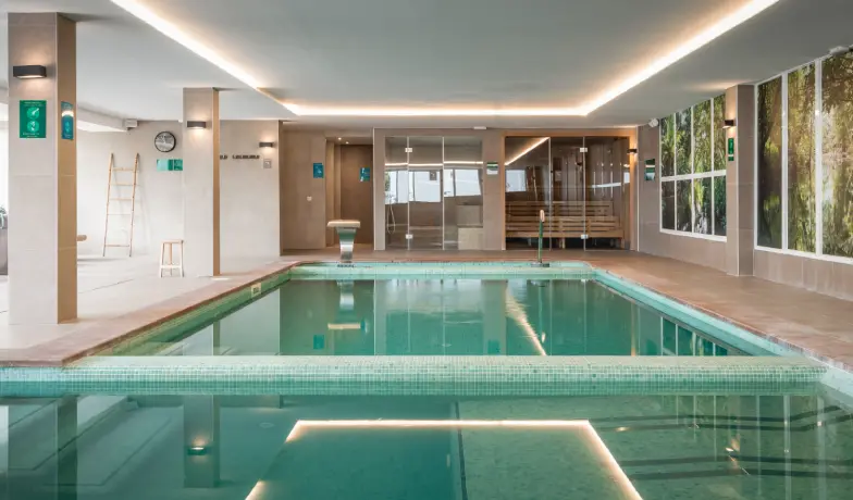 Piscina cubierta de hotel con luces LED y paredes de cristal.