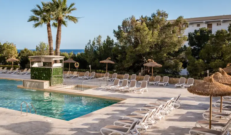 Piscina al aire libre con tumbonas y palmeras junto al mar.