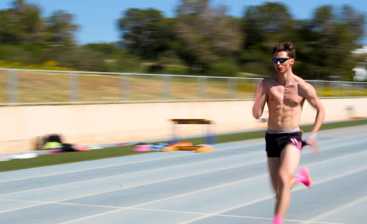 Atleta corre en una pista de atletismo al aire libre, con casco y gafas.