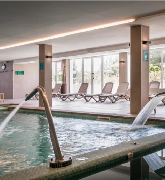 Piscina interior con chorros y tumbonas en el &aacute;rea de spa.