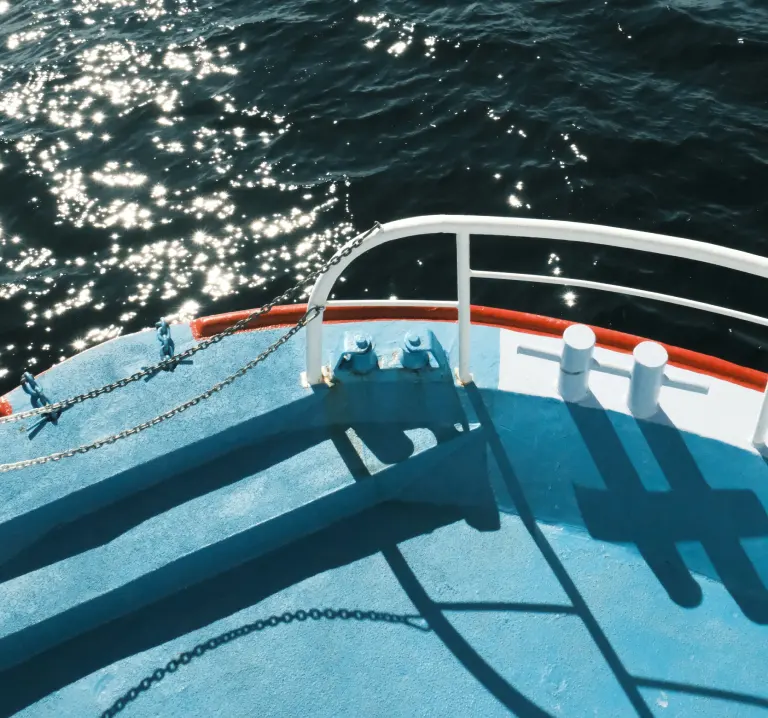 Proa de un barco sobre el mar, con el agua brillante al atardecer