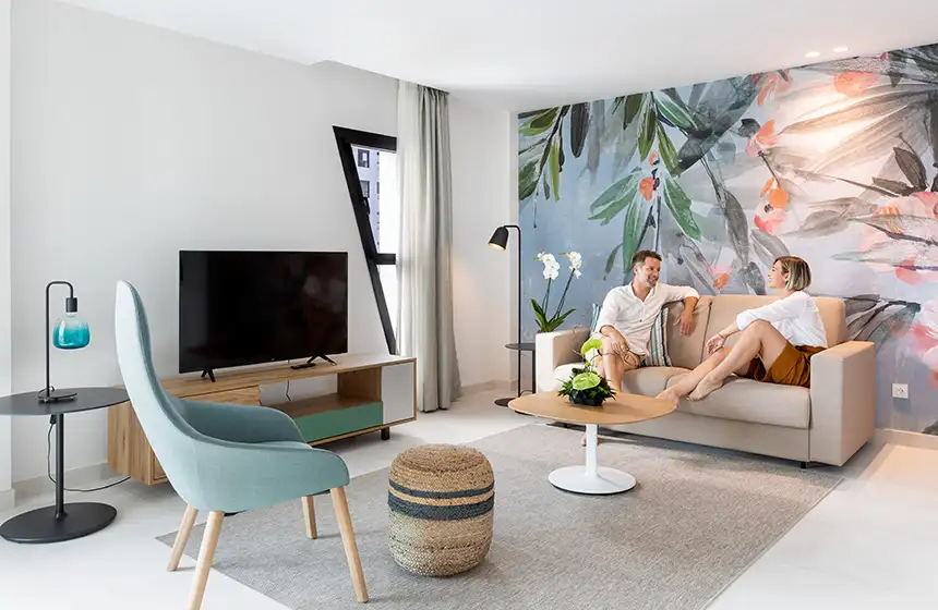 Sala de estar moderna con sof&aacute;, TV, l&aacute;mpara y pareja conversando.