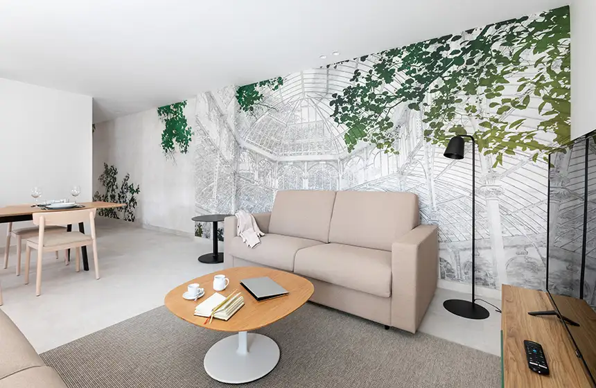 Sala moderna blanca con sof&aacute; beige, mesa redonda y pared con mural verde
