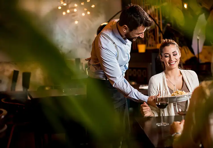 Camarero sirve vino a una mujer en un restaurante con luz c&aacute;lida.