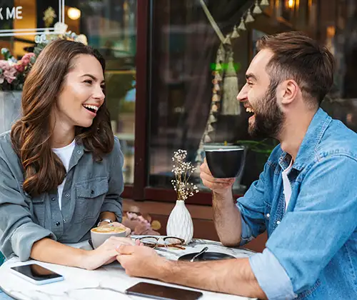 Pareja sonriente frente a copa y velas en una cena al aire libre