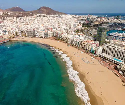 Playa urbana con mar turquesa y edificios costeros frente al puerto.
