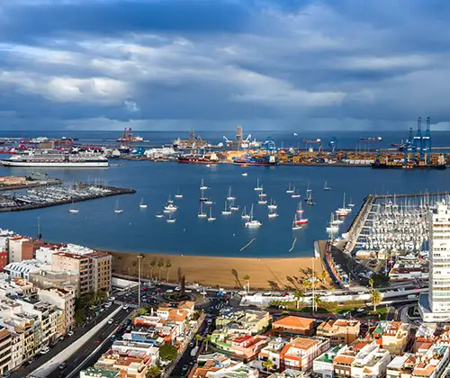 Puerto mar&iacute;timo con barcos, yates y gr&uacute;as bajo un cielo nublado.