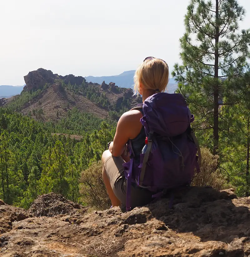 Senderista con mochila, mirando monta&ntilde;as y bosque desde un mirador rocoso.