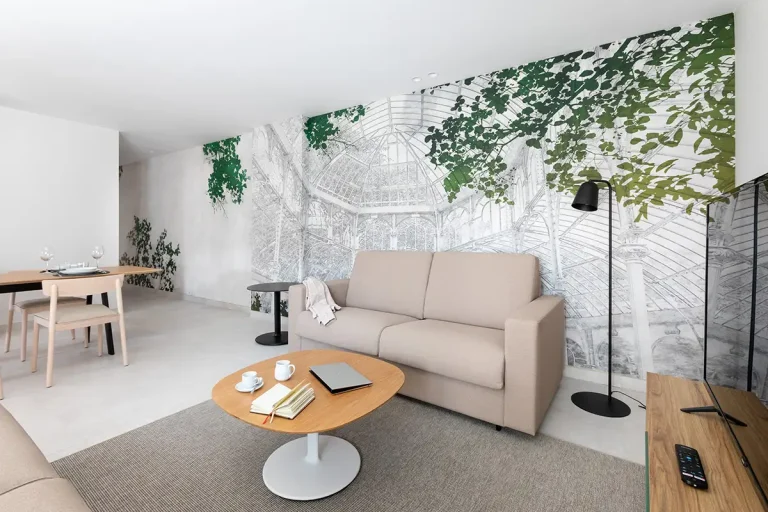 Sala moderna con sof&aacute; beige, mesa redonda y mural con enredaderas verdes