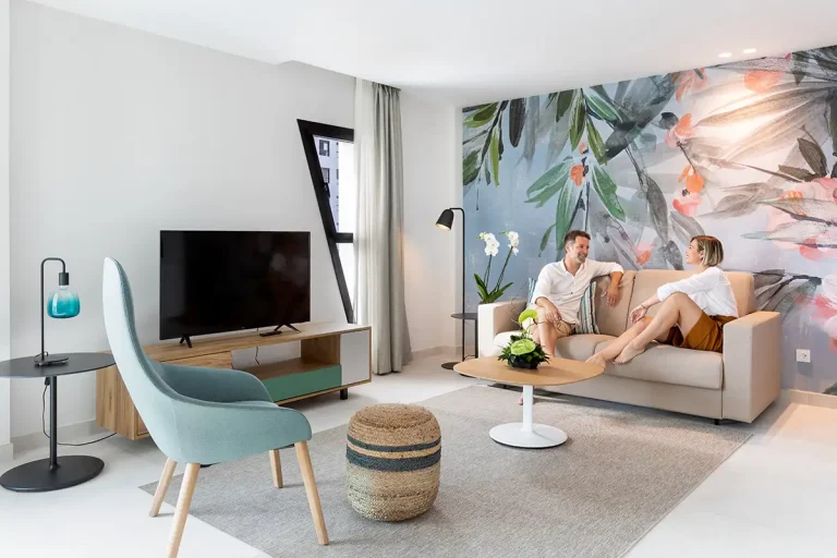 Sala moderna con sof&aacute; beige, televisor y dos personas conversando