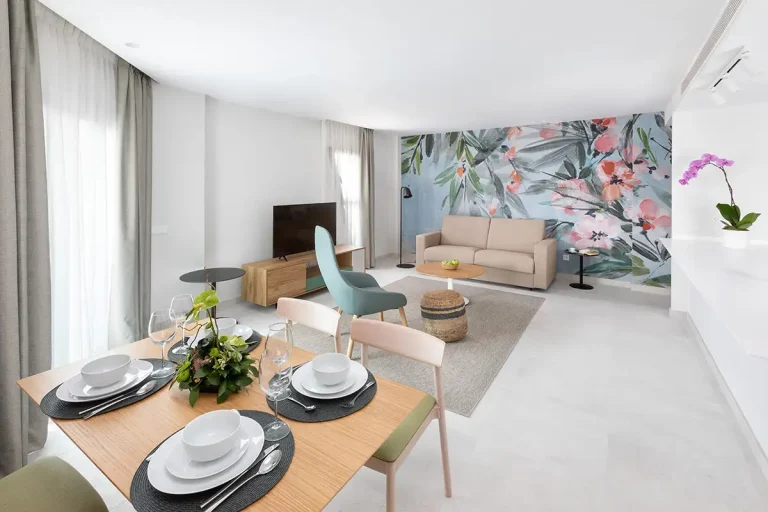 Sala moderna con mesa puesta y sof&aacute; beige, pared con mural floral