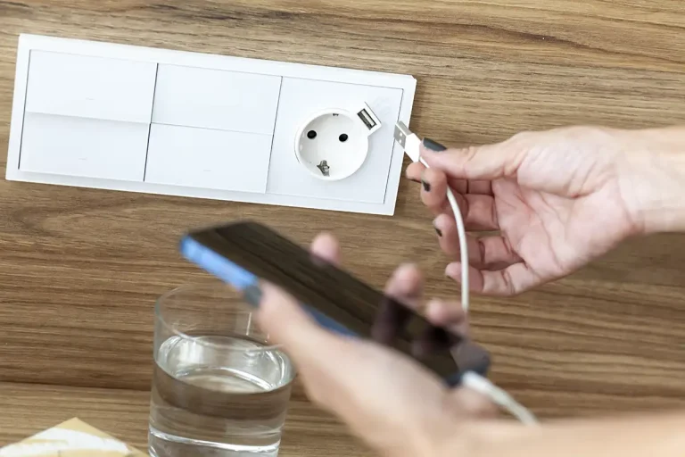 Mano enchufando un cable USB en un tomacorriente de pared con varios m&oacute;dulos