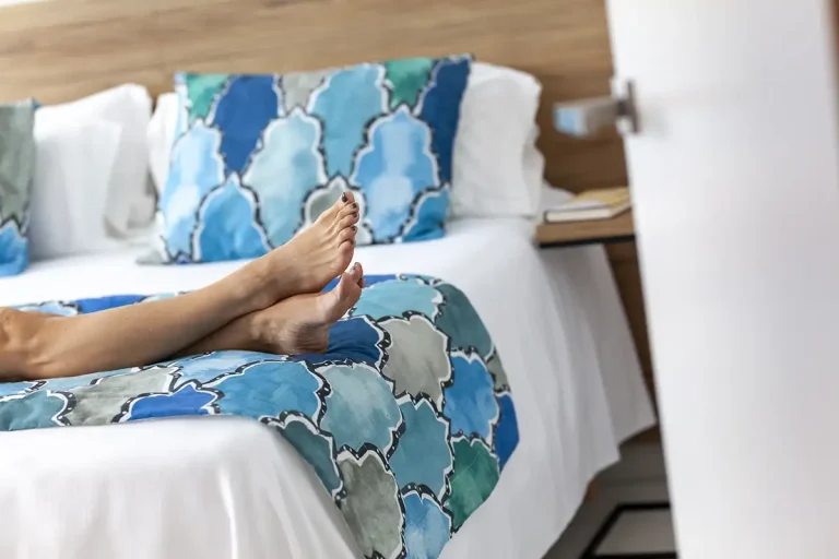 Persona relaj&aacute;ndose en una cama con s&aacute;banas estampadas azules y pies visibles